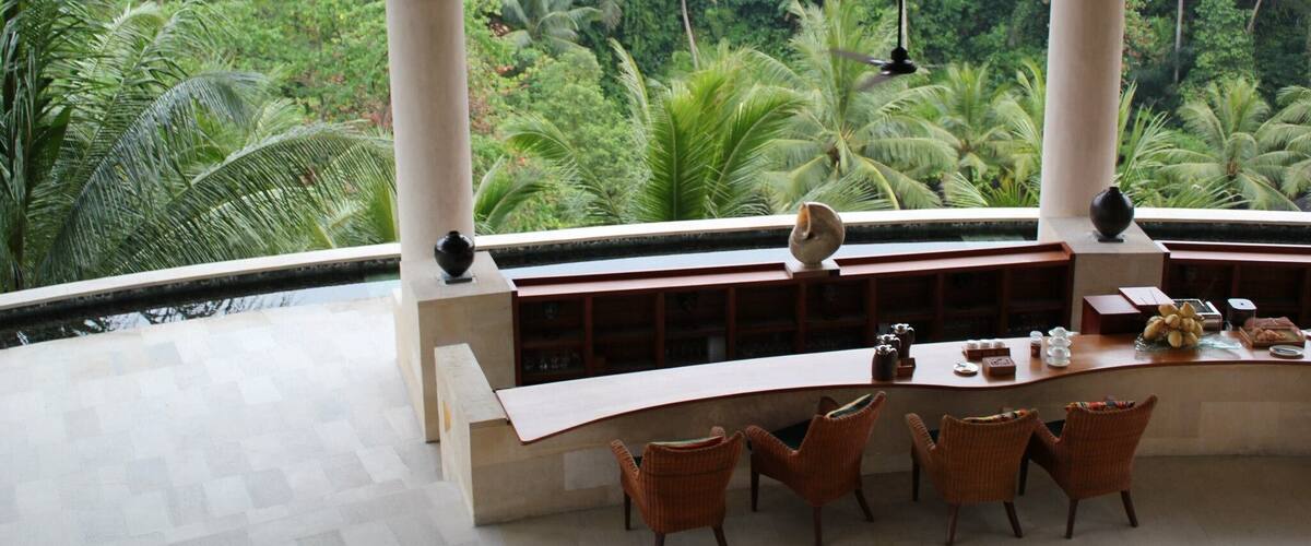 A modern interior with a curved reception desk, wicker chairs, and a view of a lush tropical forest.