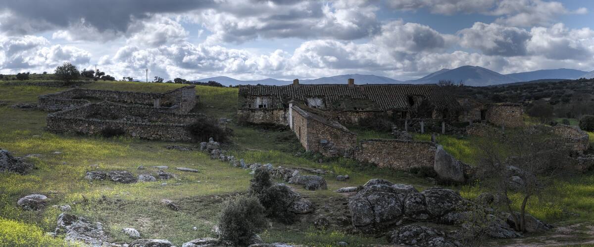 Ancient stone ruins, a dirt path, and a mountainous landscape under a cloudy sky.