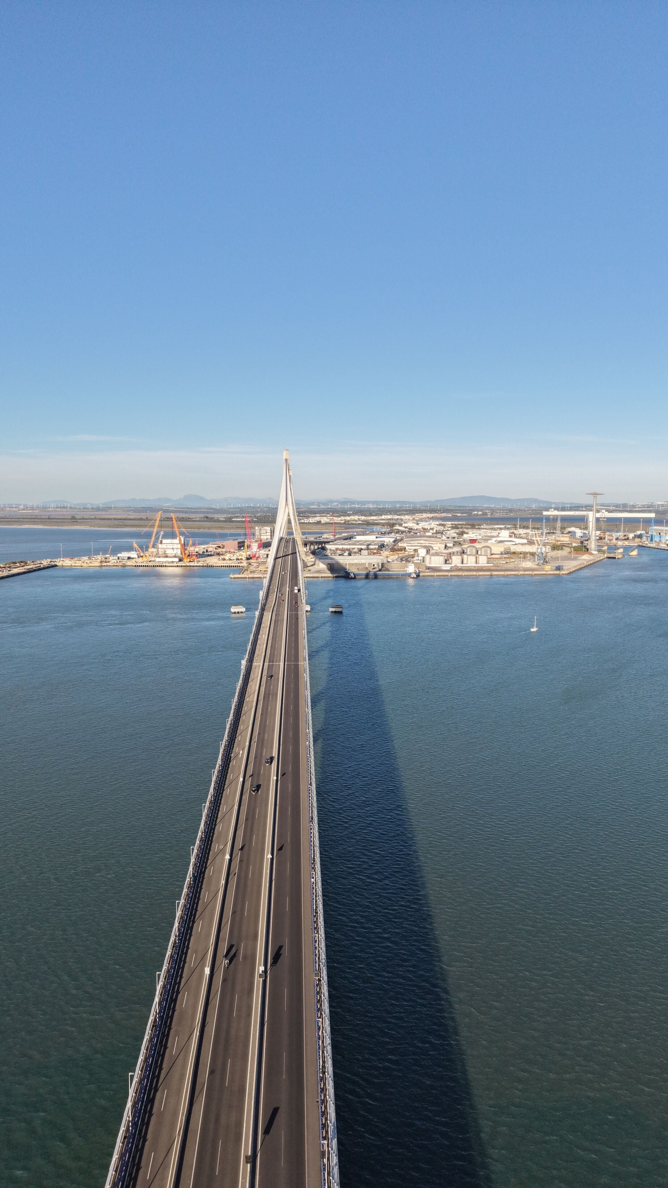 A long bridge spanning a body of water with industrial structures in the background.