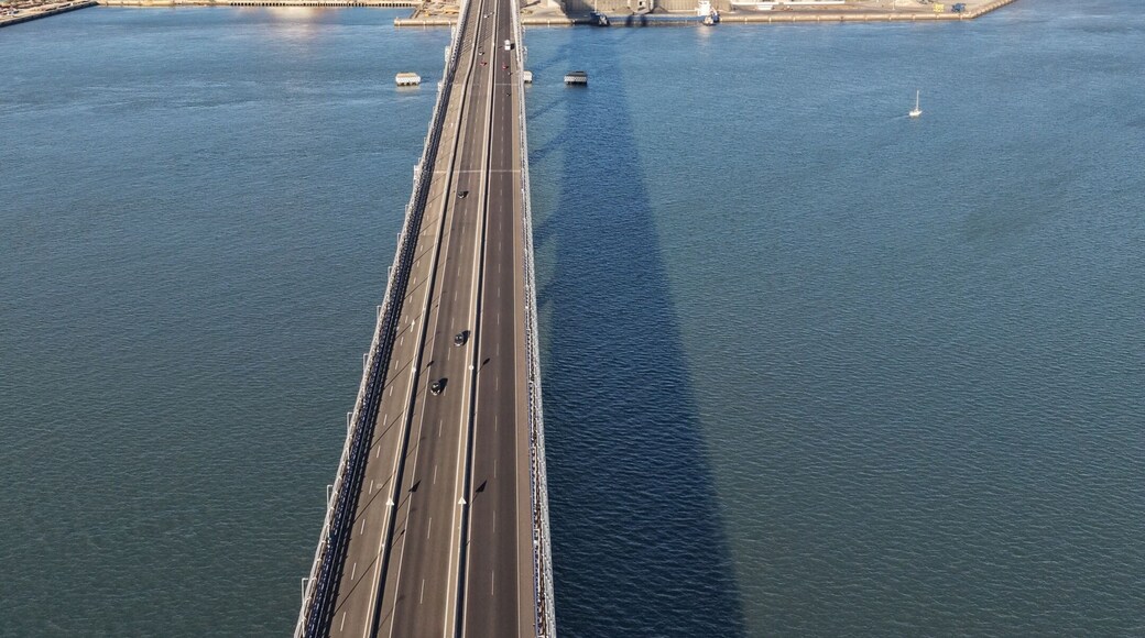 A long bridge spanning a body of water with industrial structures in the background.