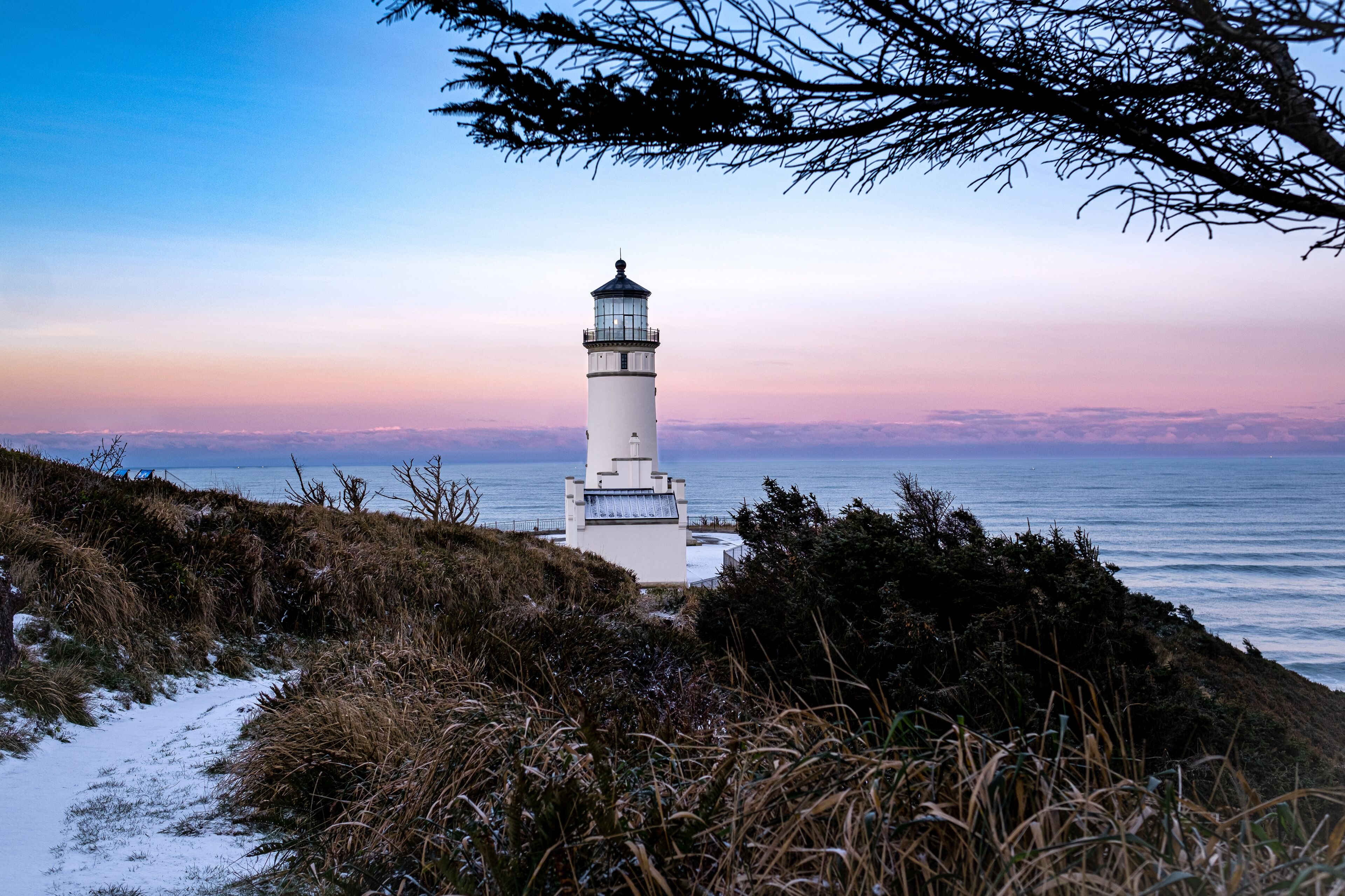 A lighthouse on a coastal cliff with a view of the ocean and a sunset sky.