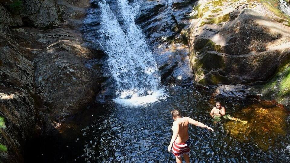 A waterfall in a rocky terrain with a person swimming in the water.