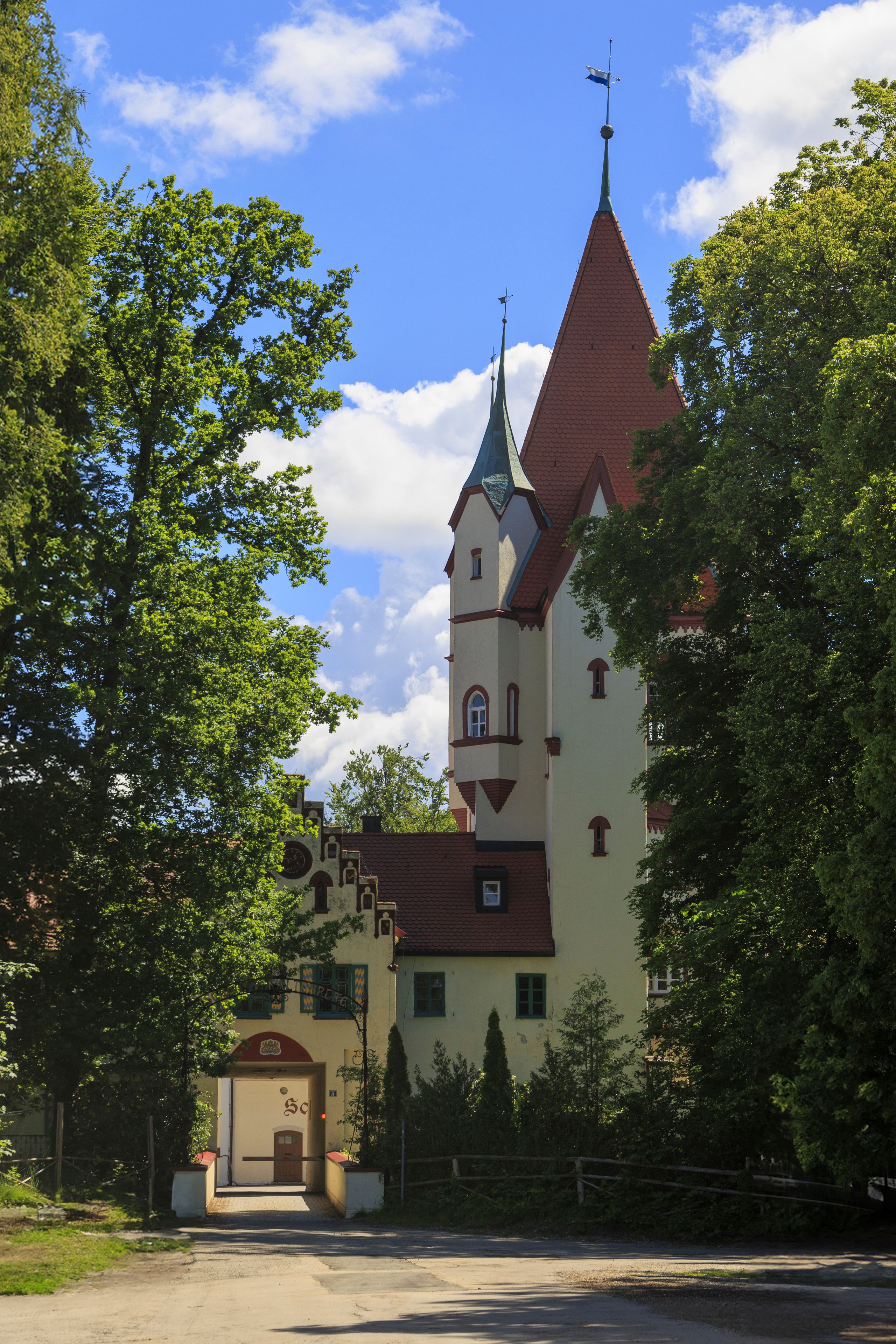 A castle with a red roof and a tall tower, surrounded by lush green trees.