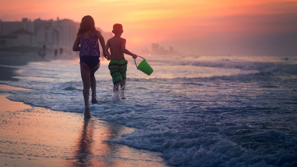 Siblings paddling in sea at sunset, North Myrtle Beach, South Carolina, United States