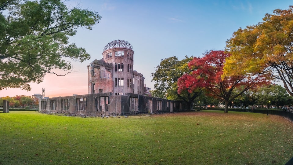 The Atomic Bomb Dome Panorama in Hiroshima and the surounding garden in autumn at sunset on the side of Motoyasu River in Japan, with the Peace Memorial Park on the left in the background.