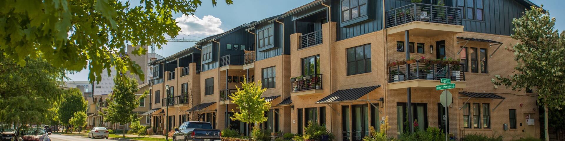 A multi-story residential building with balconies, a street with cars, and trees.