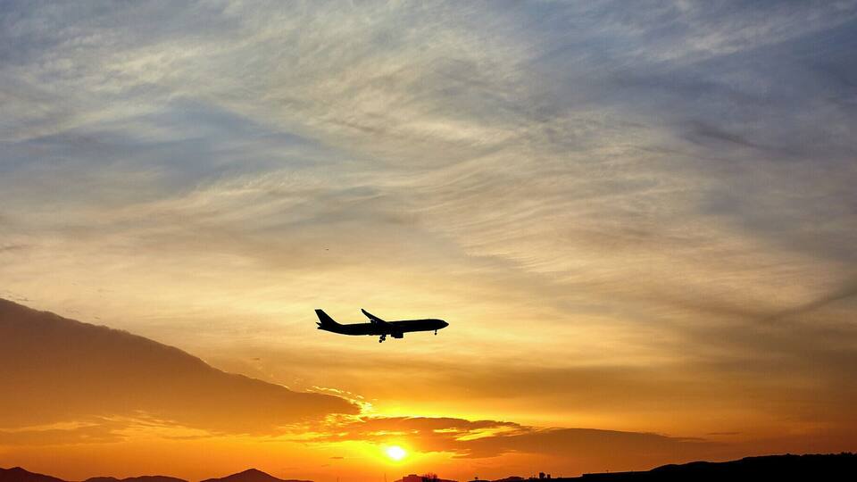 An airplane flying during sunset with a mountain range in the background.