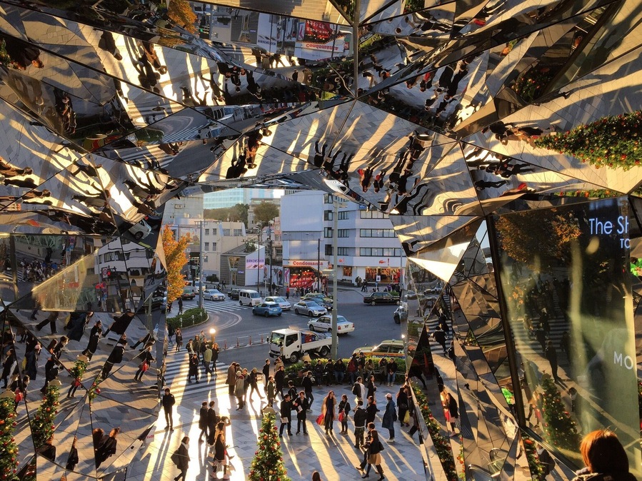 A busy urban street with a large glass structure reflecting the surroundings.