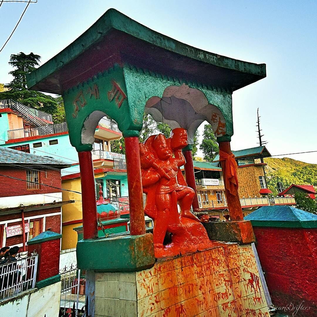 A colorful statue under a green shelter with inscriptions.