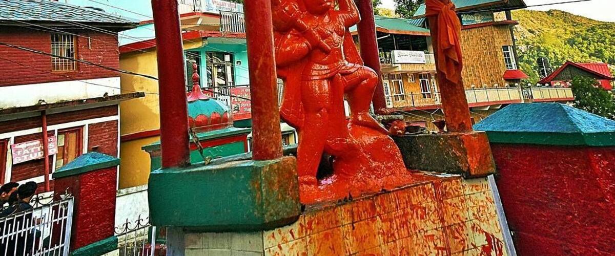 A colorful statue under a green shelter with inscriptions.