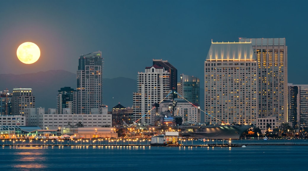 A city skyline with a prominent moon in the sky and a large ship docked at the waterfront.