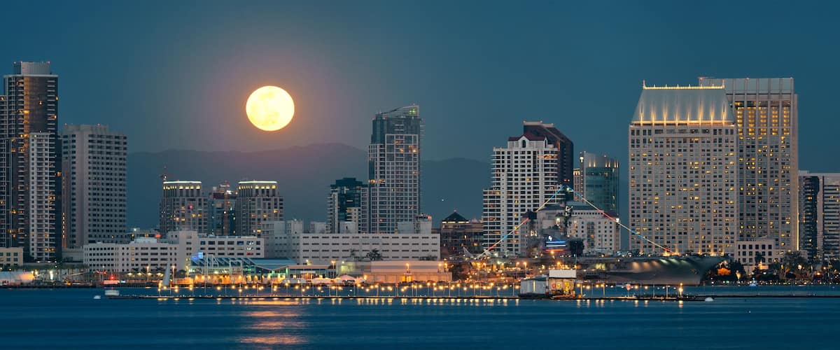 Un horizonte urbano con una luna destacada en el cielo y un gran barco amarrado en el muelle.