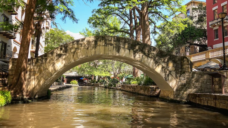 A stone bridge over a canal with buildings and trees around.