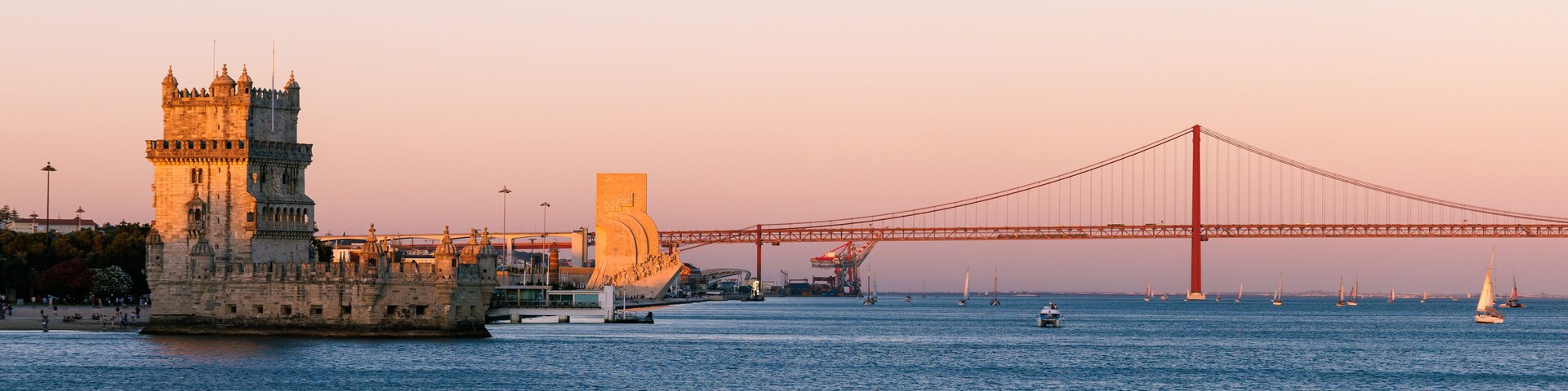 Panorama of Belém in Lisbon, the capital of Portugal. Sunset over Tagus river. Cityscape with Torre de Belém, Belém Tower and red iconic 25 de Abril Bridge, 25th of April Bridge.