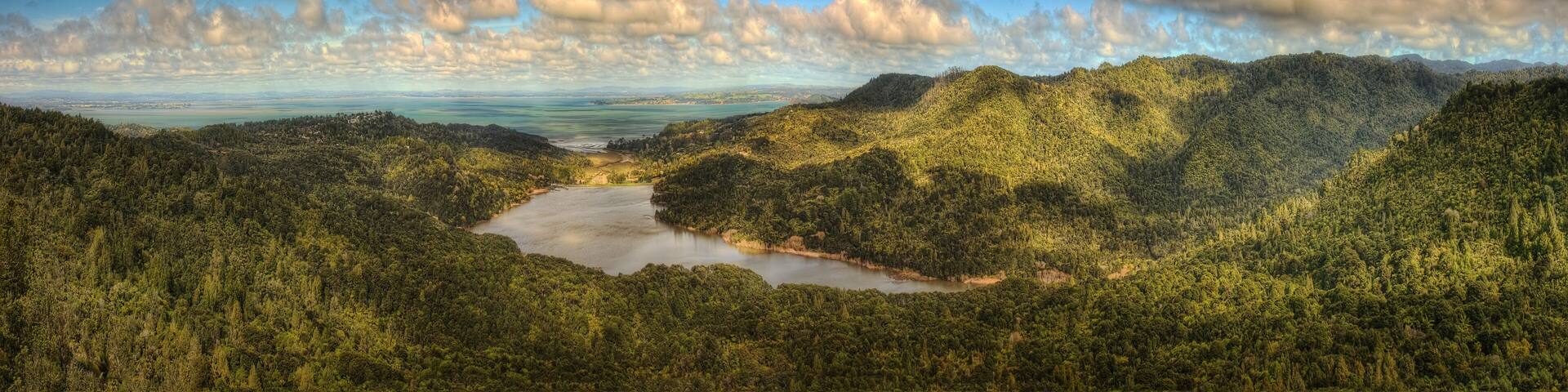 A river winding through a densely forested valley with mountains in the background and a partly cloudy sky.