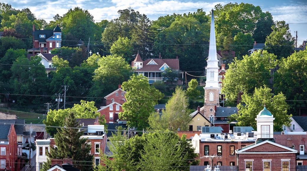 A town with historic buildings, a prominent church steeple, and lush green trees.