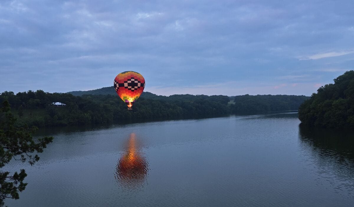 Eine Heißluftballon über einem ruhigen Fluss mit bewaldeten Ufern.