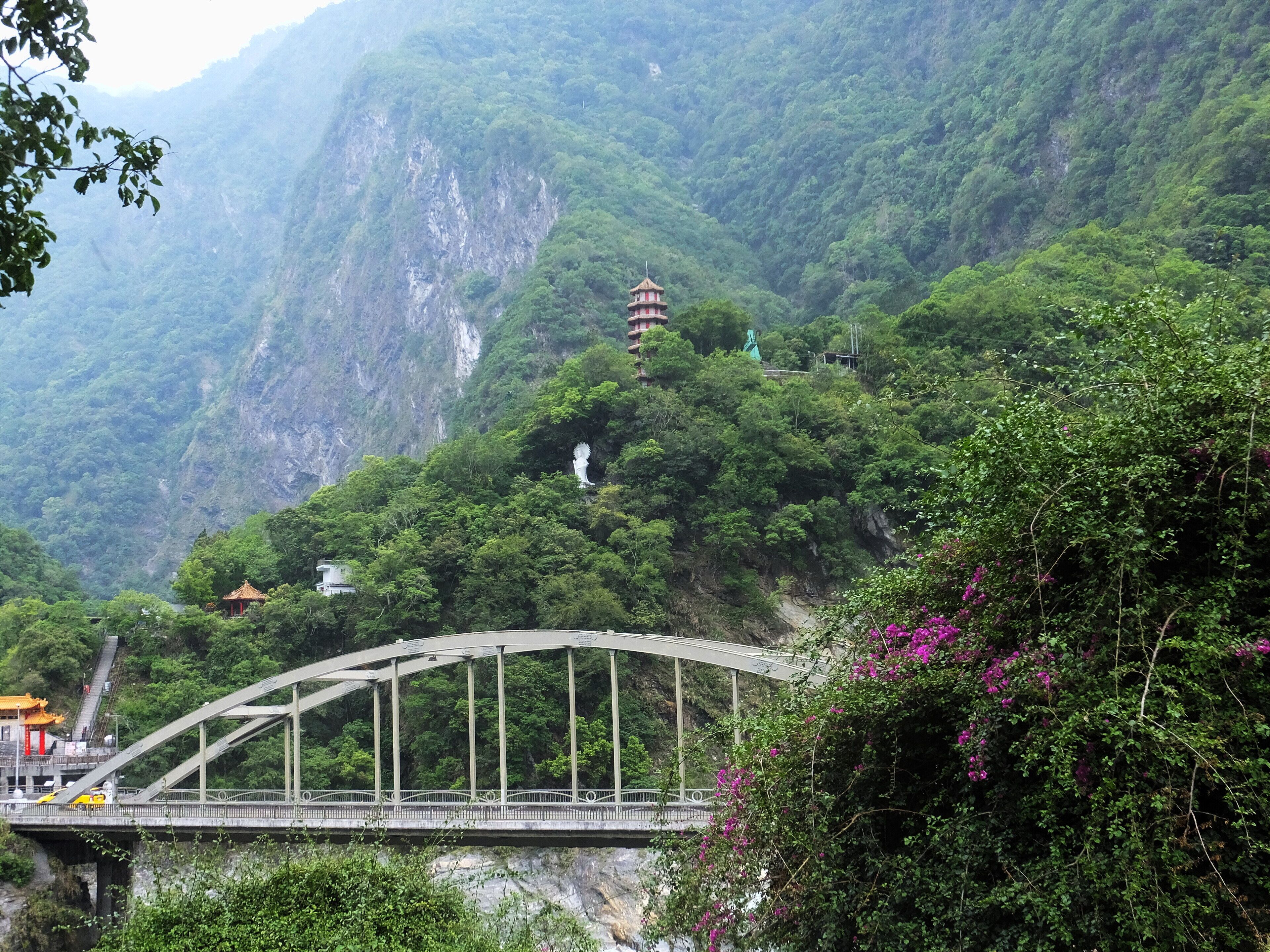 A bridge over a river, a temple on a hill, and lush green mountains.