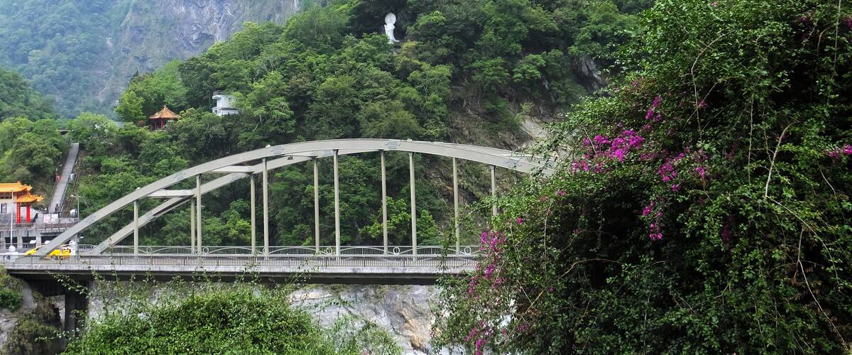 A bridge over a river, a temple on a hill, and lush green mountains.