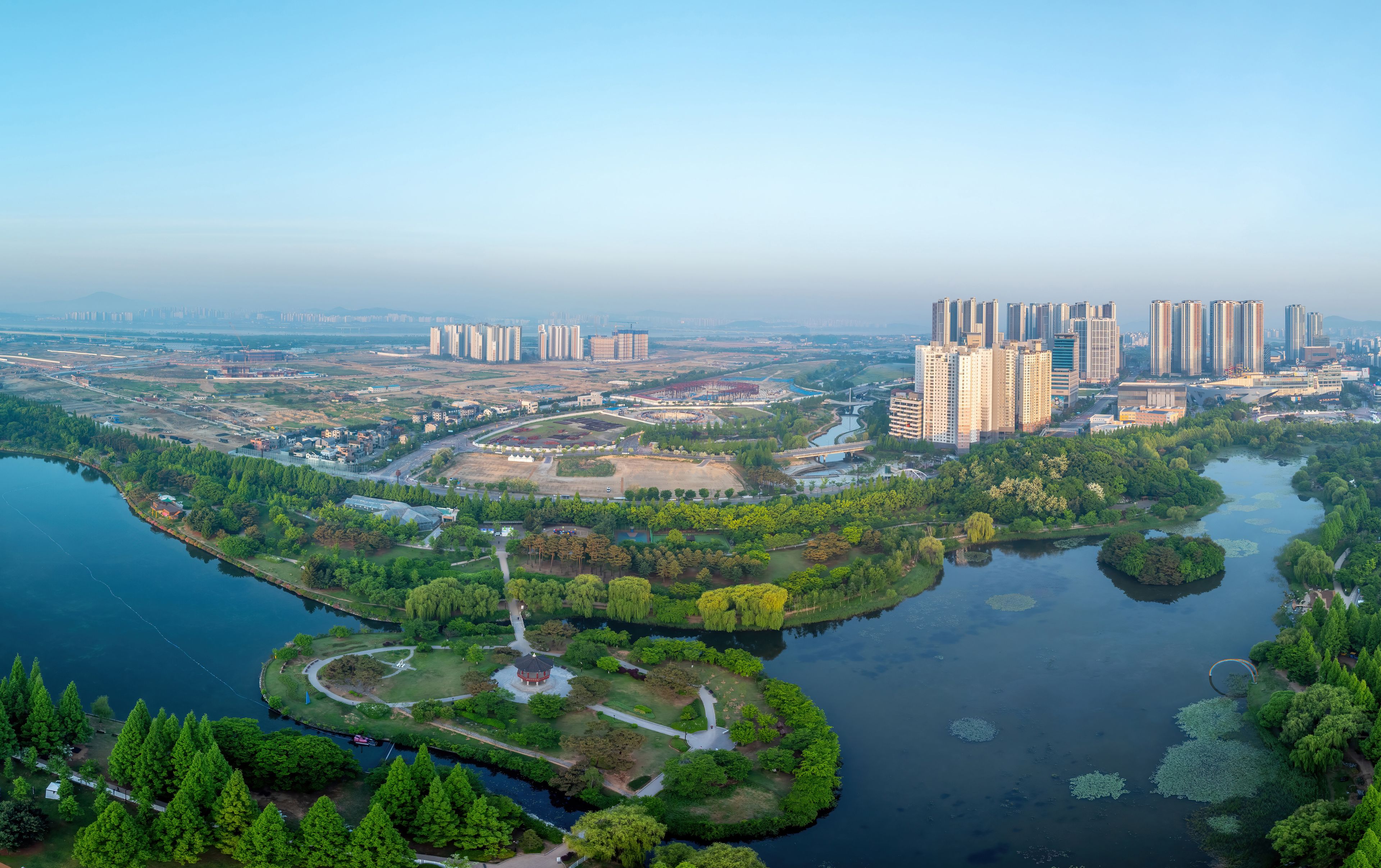 Janghang-dong, Ilsan, Goyang-si, Gyeonggi-do, South Korea - May 4, 2024: Aerial and spring view of trees with Moonrise Island on lake at Ilsan Lake Park against apartments