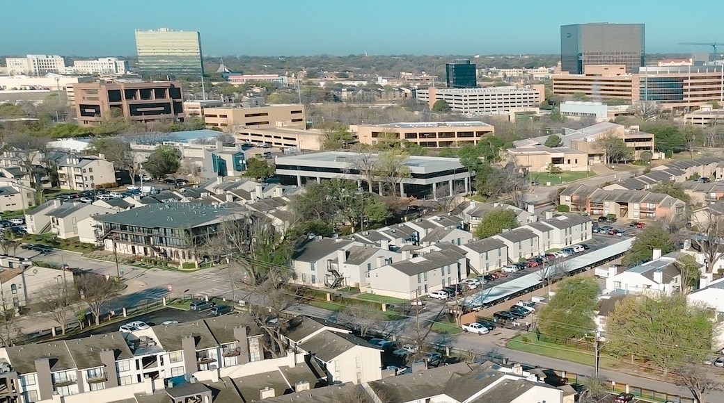 Panorama aerial dense urban housing near Fair Oaks Ave and Holly Hill Dr reveals tightly packed apartments leading toward commercial towers horizon. Brown roofs, parked cars, midtown Dallas, TX
