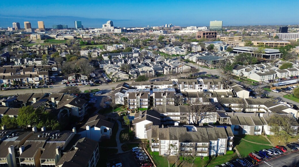 Multifamily–skyline approach near Fair Oaks Ave, Pineland Dr highlights residential clusters extending toward rising office buildings. Light exteriors, patterned roofs, muted foliage rest, Dallas