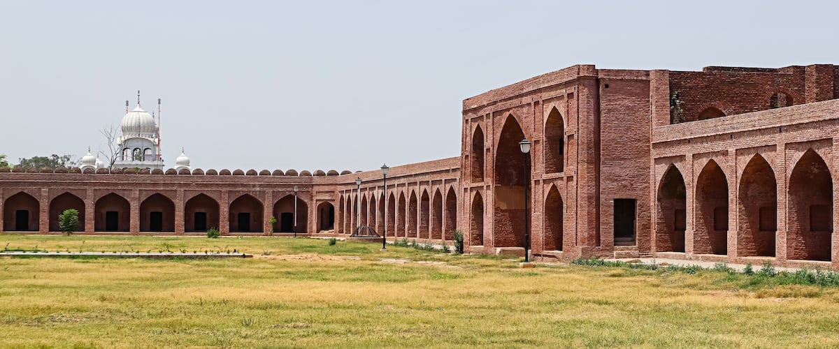 A large open courtyard with a brick building featuring arched walkways and a white domed structure in the background.
