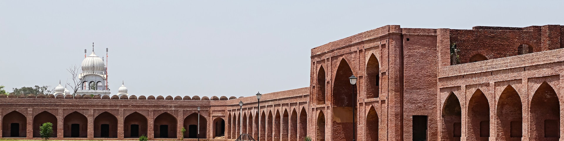 A large open courtyard with a brick building featuring arched walkways and a white domed structure in the background.