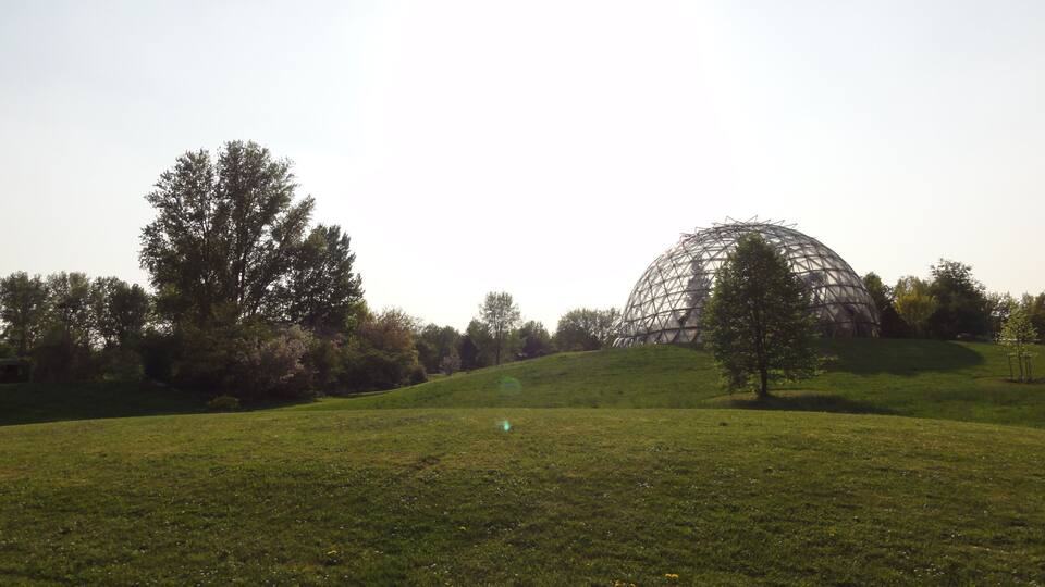 A large geodesic dome structure on a grassy hill with trees in the background.