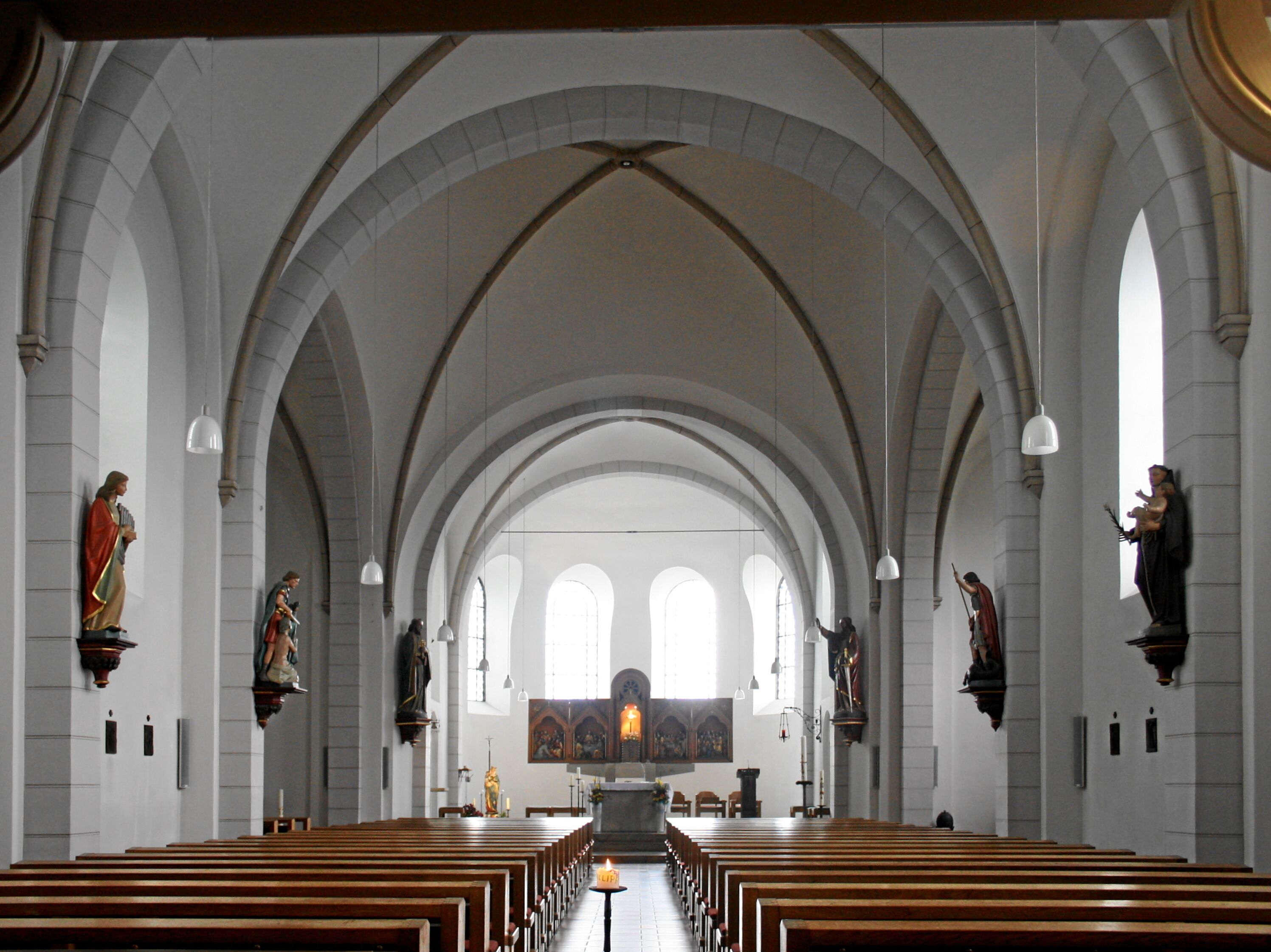 A church interior with arched ceilings, wooden pews, and religious statues.
