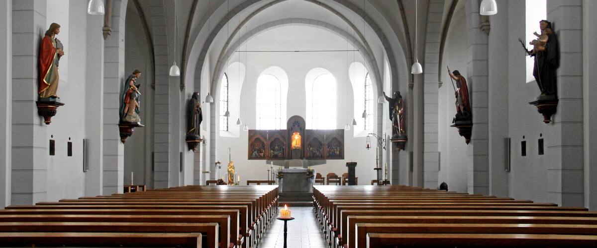 A church interior with arched ceilings, wooden pews, and religious statues.