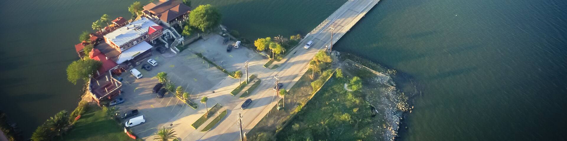 An aerial view of a river with a bridge, a parking lot, and buildings along the riverbank.