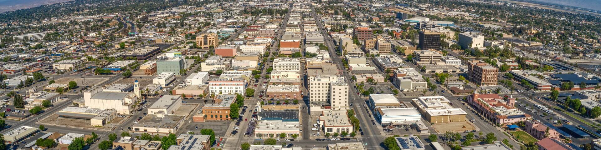 An aerial view of a city with a grid of streets, buildings, and distant mountains.