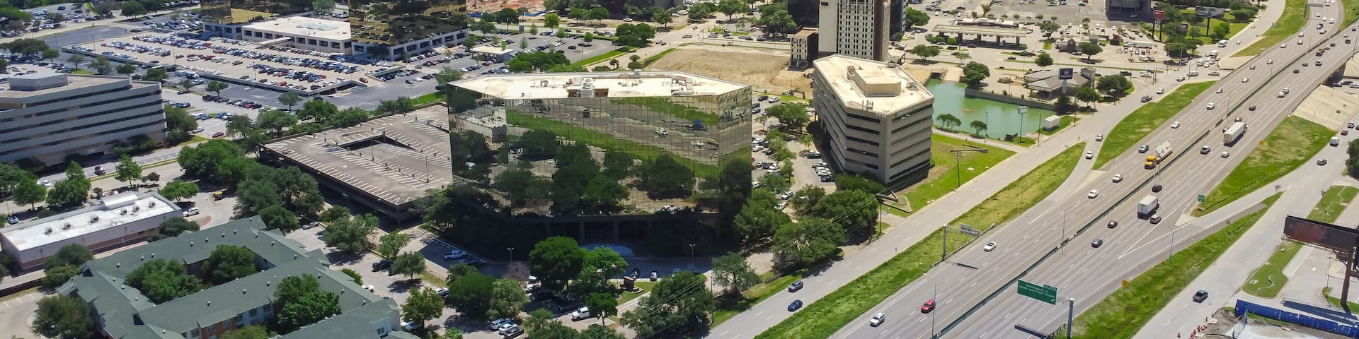 Business park group of office buildings, hotels, restaurants in Love Field neighborhood with downtown Dallas in background, sunny clear blue sky, busy traffic on Stemmons Freeway I35, aerial view