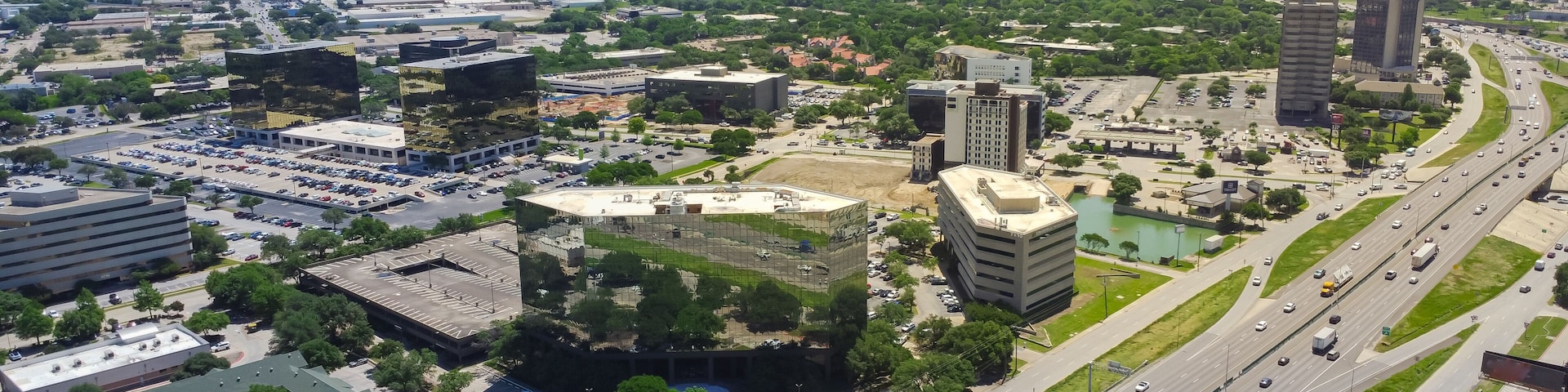 Business park group of office buildings, hotels, restaurants in Love Field neighborhood with downtown Dallas in background, sunny clear blue sky, busy traffic on Stemmons Freeway I35, aerial view