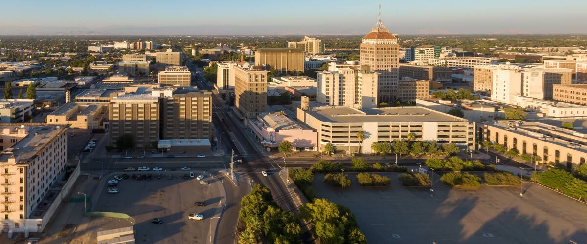 Aerial view of downtown Fresno, California, USA, at sunrise. The image shows the city's skyline, including the historic Pacific Southwest Building, and surrounding urban landscape.
