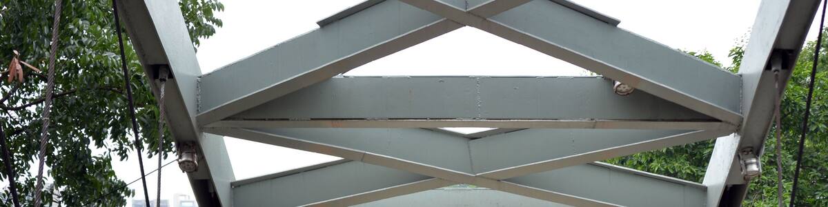 A pedestrian bridge with a metal framework and wooden walkway, overlooking a river and dense greenery.