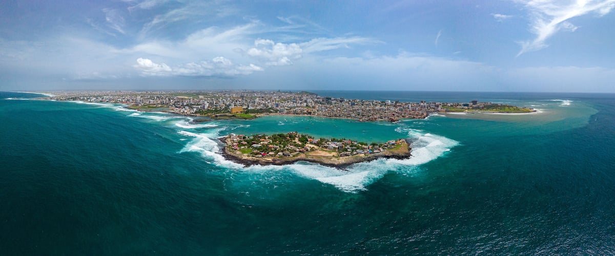 Aerial view of Ngor Island surrounded by turquoise ocean waves with the city skyline in the background in Dakar, Dakar Region, Senegal.