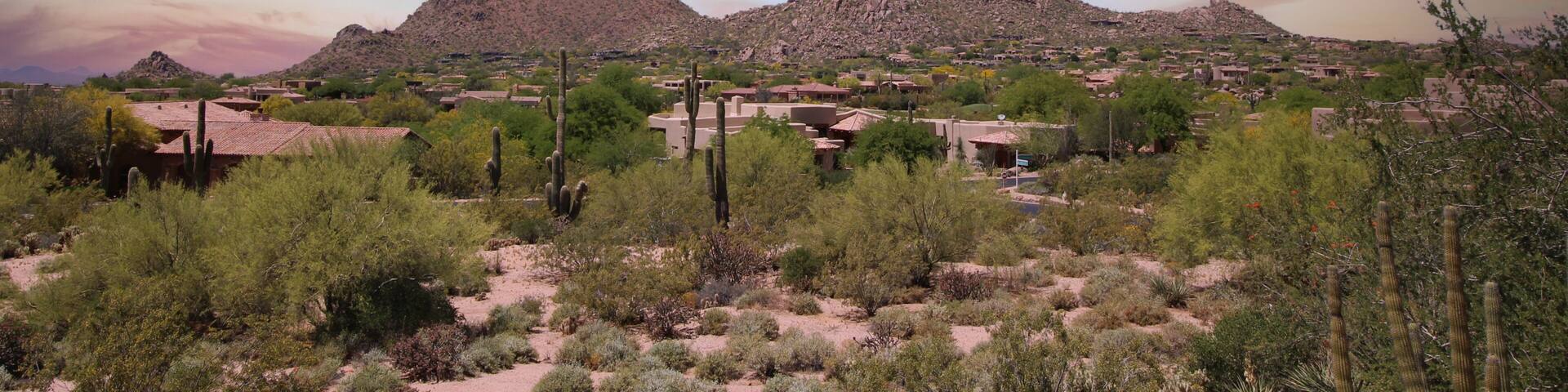 A desert landscape with two prominent mountains, sparse vegetation, and a small settlement in the foreground.