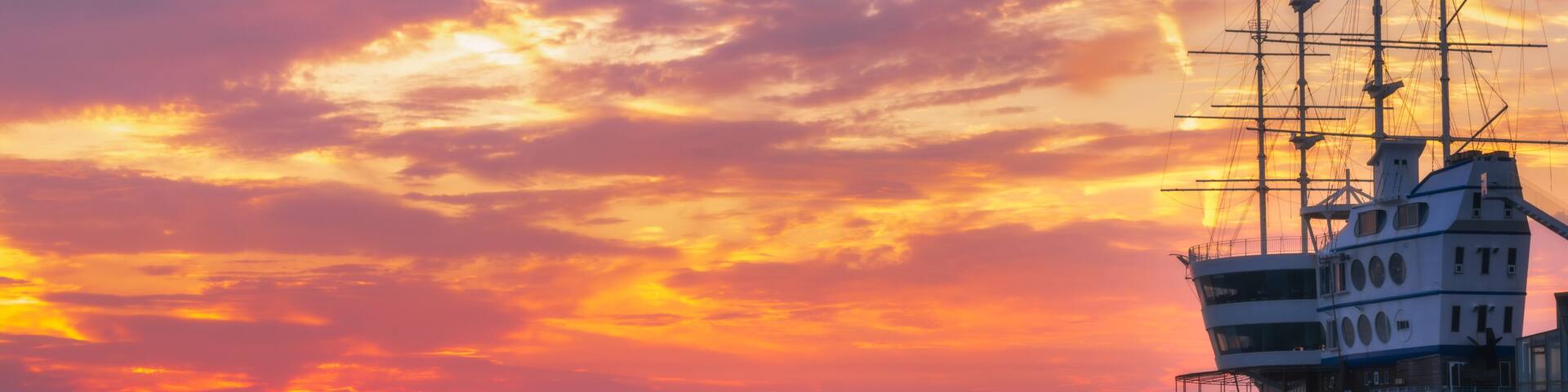 A ship at sunset with a colorful sky and rocky coastline.