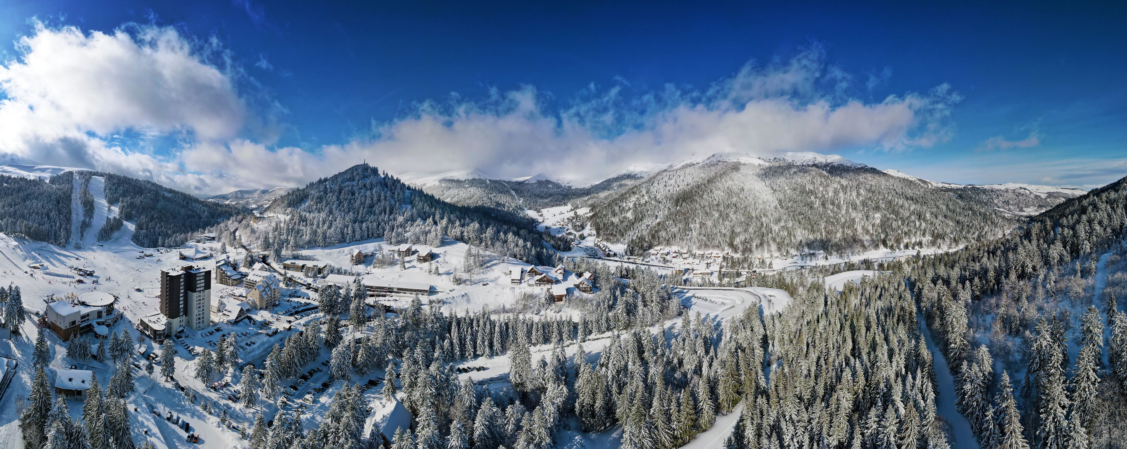 A snow-covered mountain landscape with ski slopes, buildings, and dense forests.