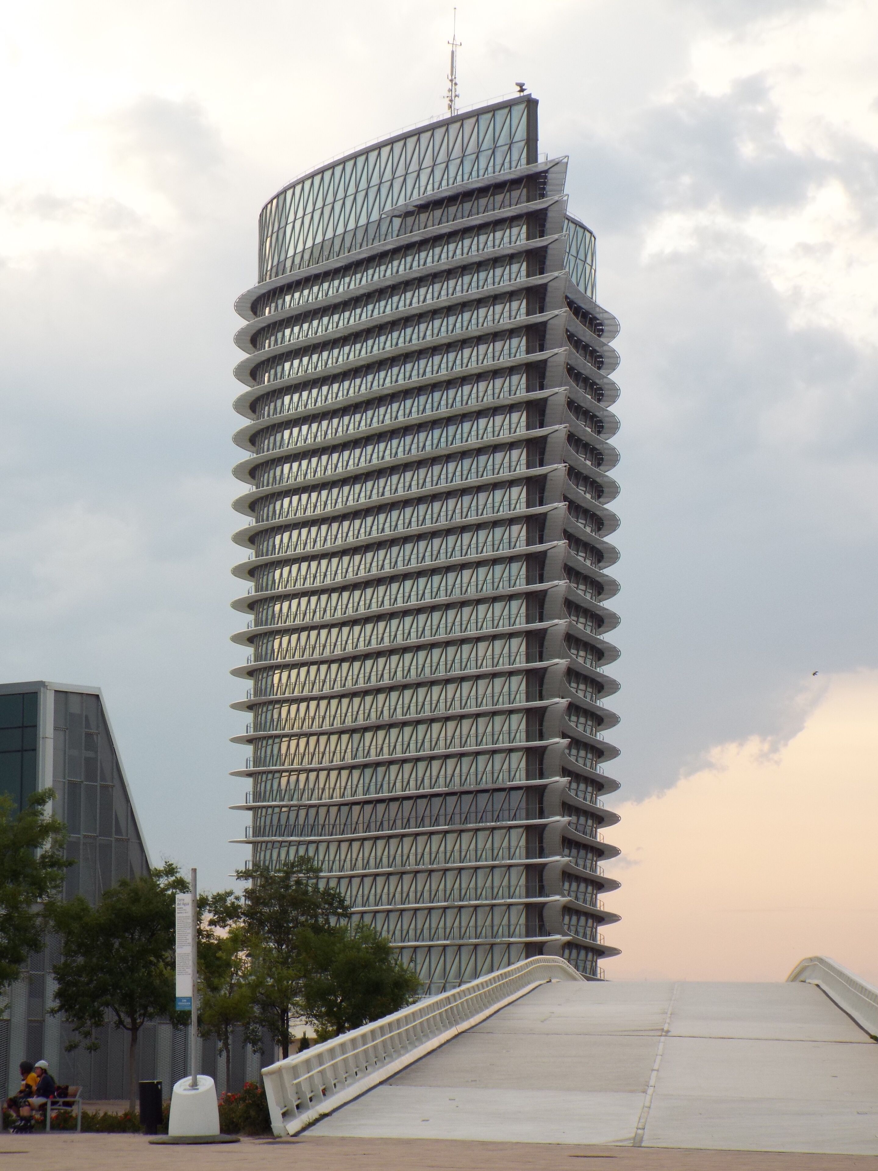 A modern skyscraper with a unique spiral design, surrounded by a park with benches and trees.