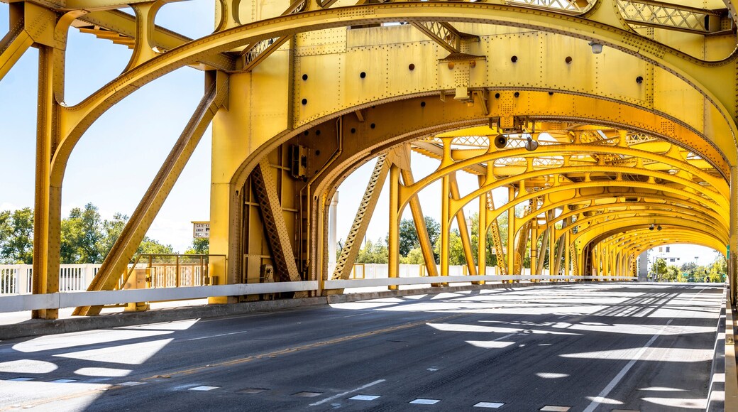 Glowing in the sun arched truss car and pedestrian golden bridge in old Sacramento