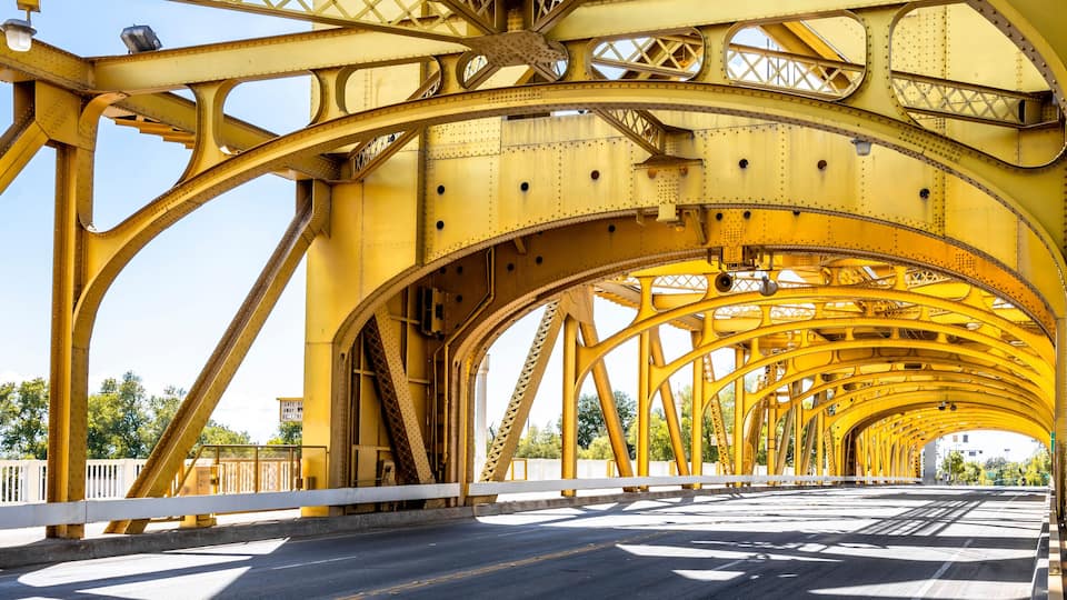 Glowing in the sun arched truss car and pedestrian golden bridge in old Sacramento