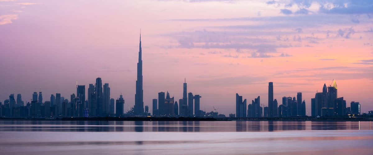 Stunning view of the Dubai skyline silhouette during sunset with the magnificent Burj Khalifa and many other buildings and skyscrapers. Silky smooth water flowing in the foreground.
