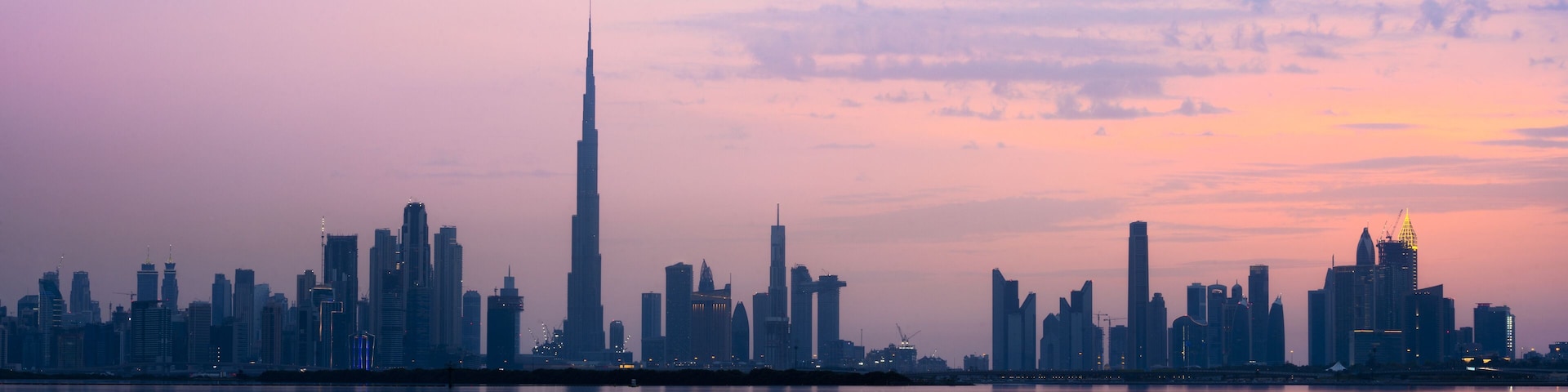 Stunning view of the Dubai skyline silhouette during sunset with the magnificent Burj Khalifa and many other buildings and skyscrapers. Silky smooth water flowing in the foreground.