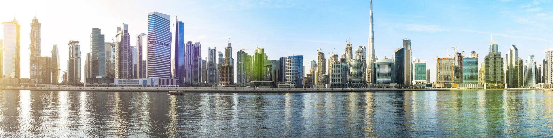 A city skyline with modern high-rise buildings and a river in the foreground.