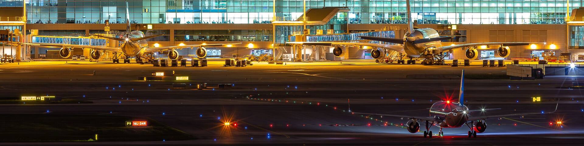 An airport with a control tower, terminal buildings, and airplanes on the tarmac at night.