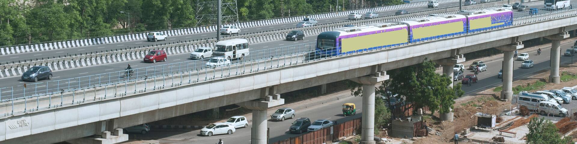 A busy highway with multiple lanes of traffic, including cars, buses, and motorcycles. There are overhead power lines and a bridge with a construction site below.