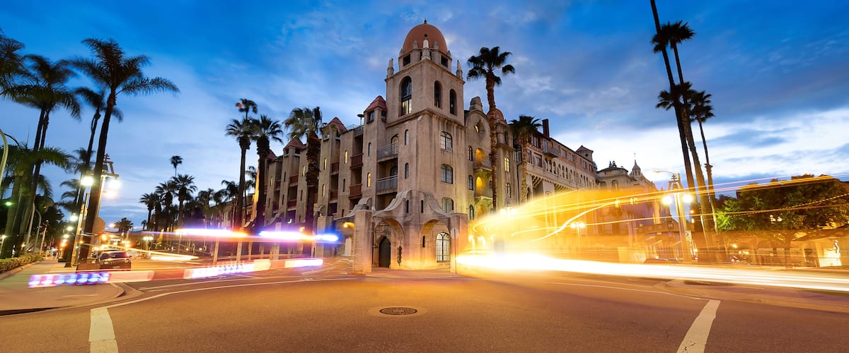 A historic building with a dome and arched windows, surrounded by palm trees and a busy street with light trails.